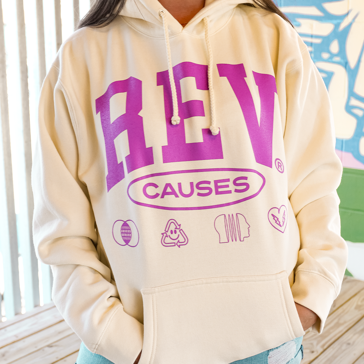 Cream-colored hoodie with purple ’REV CAUSES’ text and small icons printed on the front.