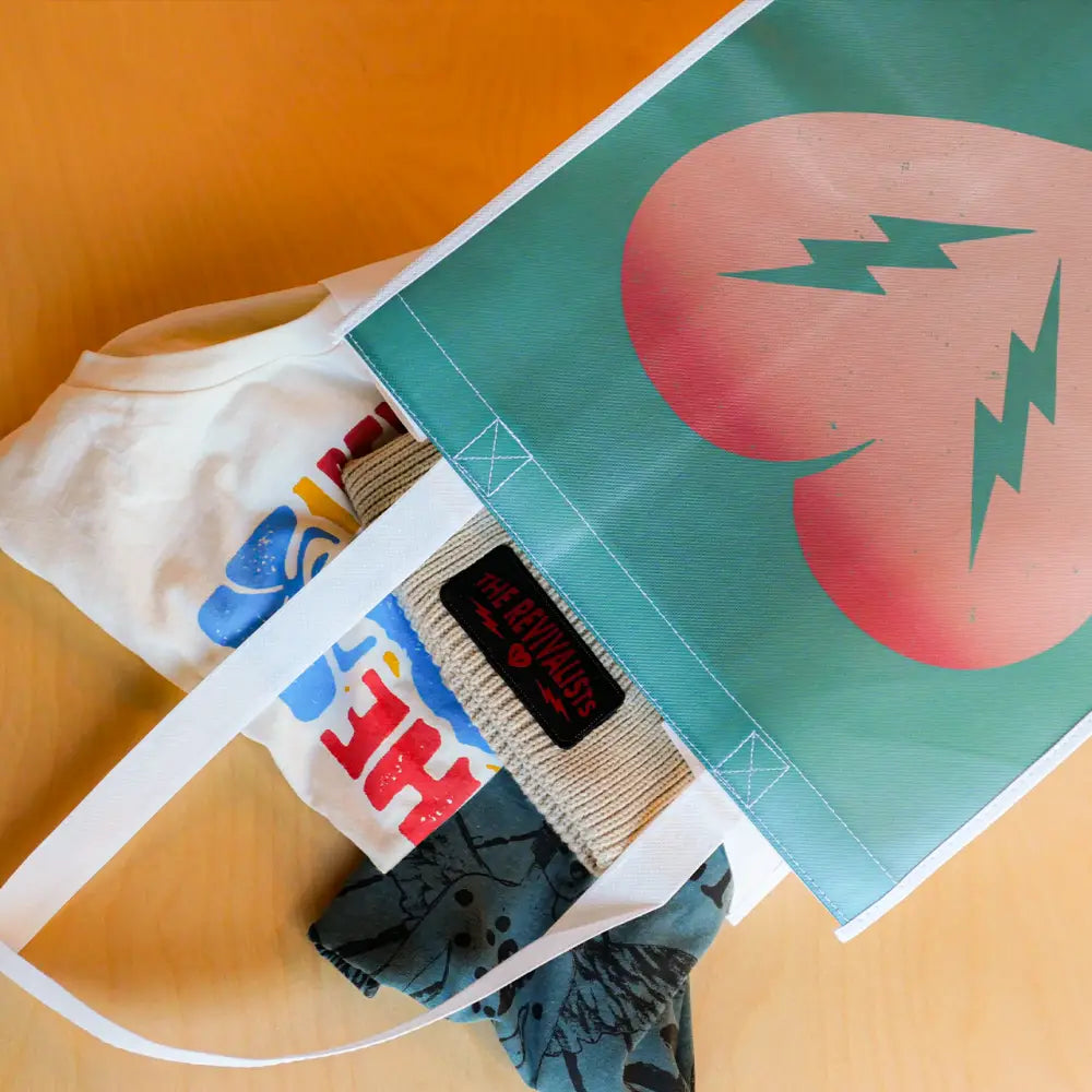 White tote bag with colorful graphic prints alongside a teal poster featuring a pink heart with lightning bolts.