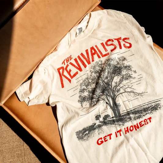 A cream cotton honest tee with a black and red tree graphic and the revivalists text across the chest