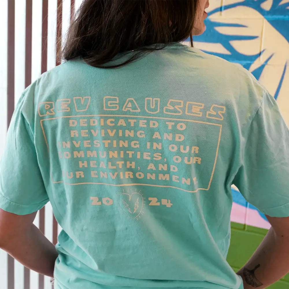 Mint green t-shirt with text about reviving and investing in communities printed on the back.