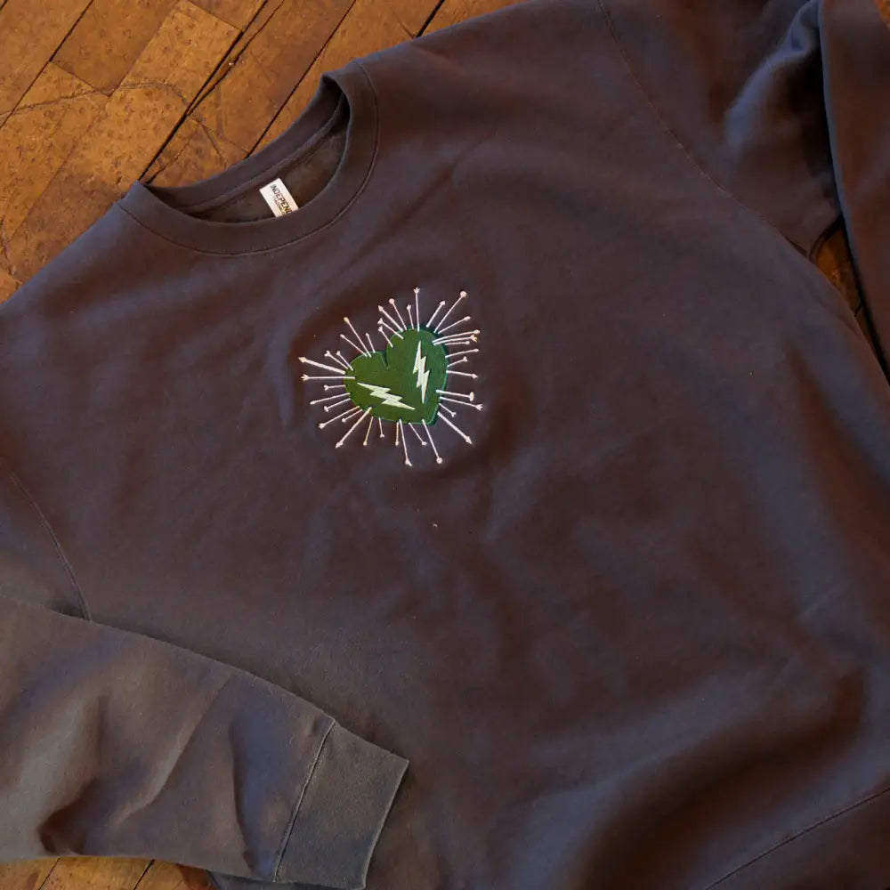 Dark gray sweatshirt featuring a green heart with a white lightning bolt and radiating silver spikes embroidered on the chest.