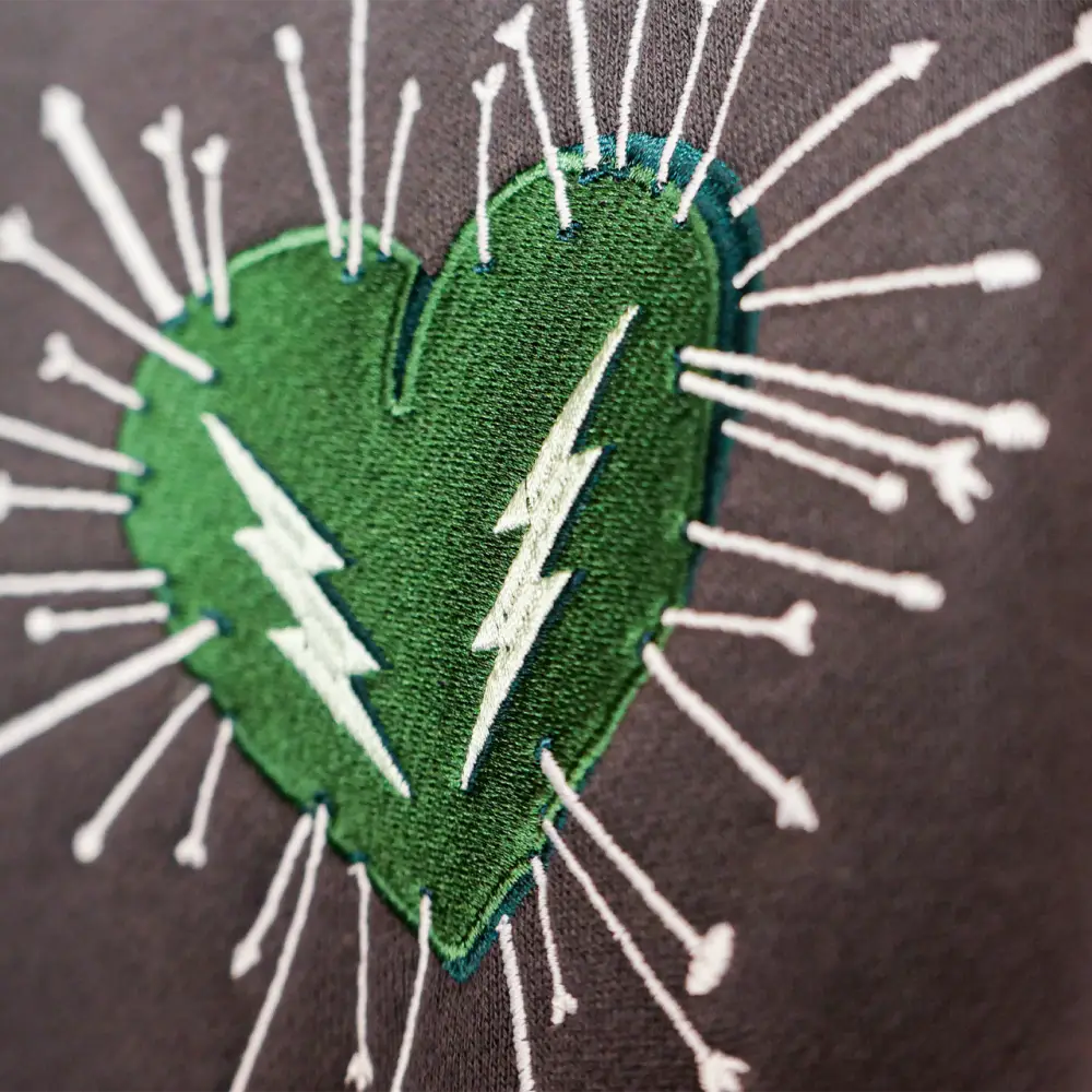 Green heart-shaped patch with white embroidered lightning bolts and radiating arrows.