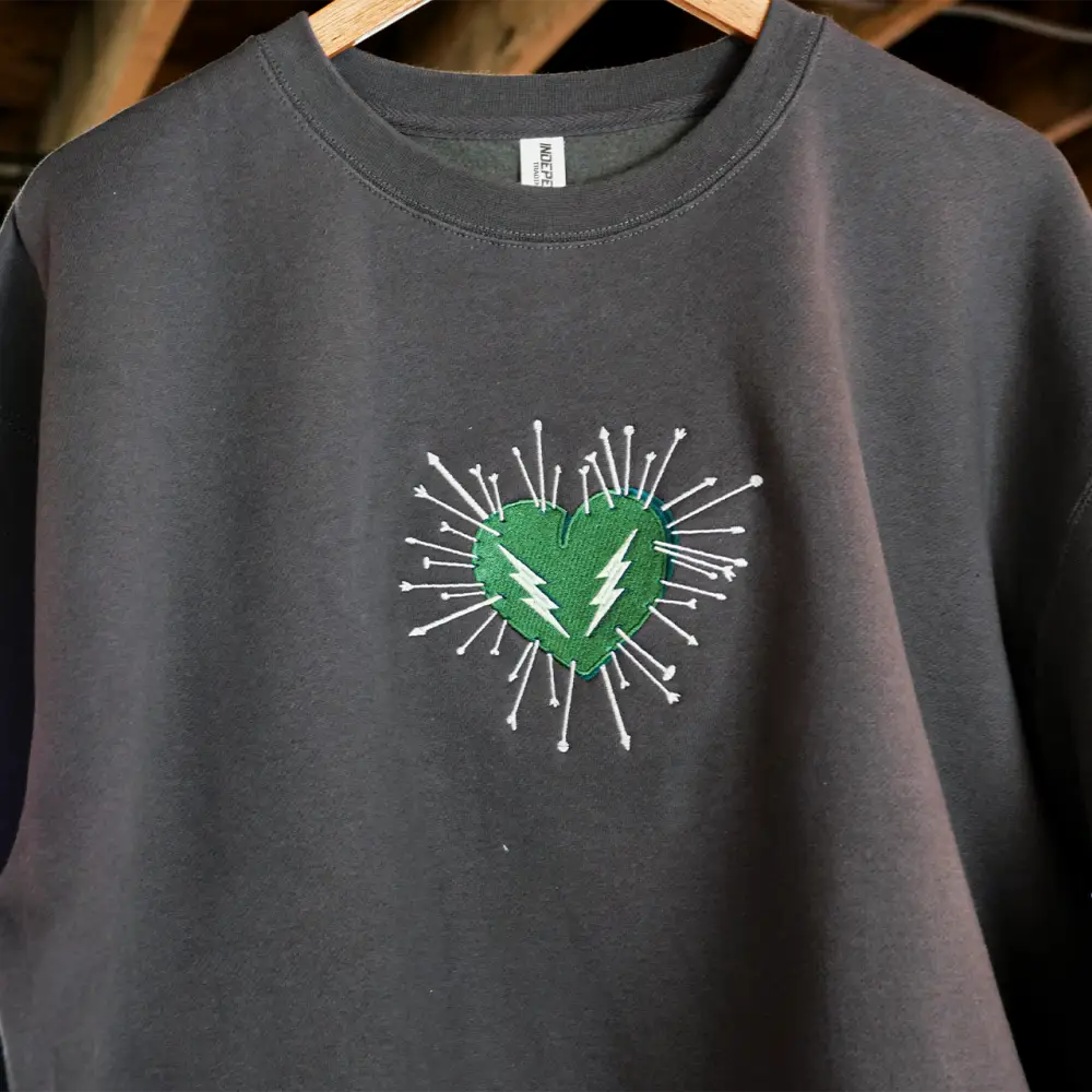 Dark gray crewneck sweatshirt featuring a vibrant green heart embroidered with white lightning bolts and radiating spikes.