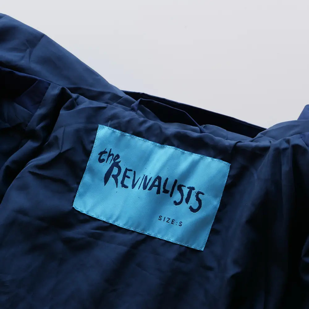 Blue clothing label with ’the REVIVALISTS’ printed on it, attached to a dark fabric garment.