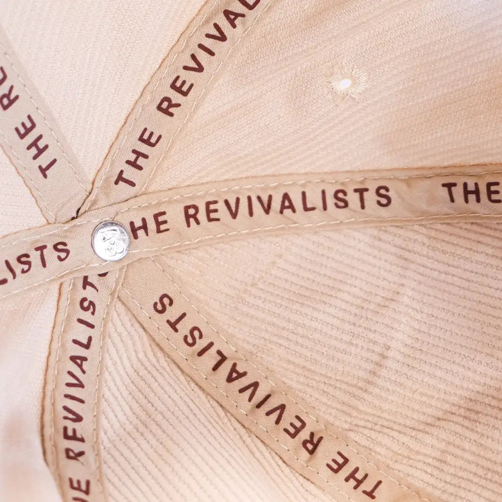 Beige baseball cap with ’THE REVIVALISTS’ text repeated around the crown.