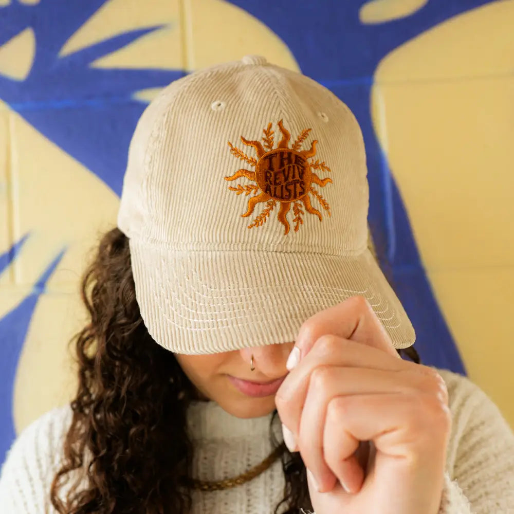 White baseball cap with an embroidered sun design on the front.