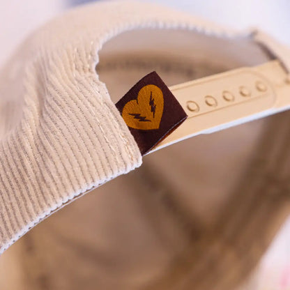 Beige baseball cap with a small brown tag featuring a yellow leaf logo.